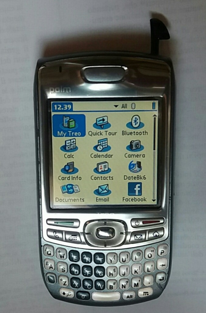A close-up of a Palm Treo smartphone displaying its main menu, featuring icons for various applications such as Calendar, Contacts, and Facebook.